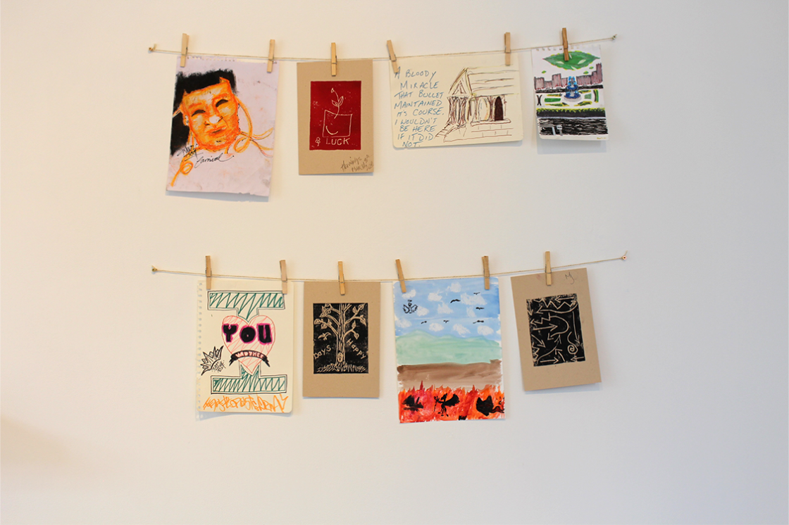 artwork hanging from clothespins from two wires on the wall 