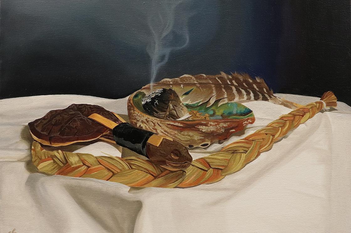 The image is a photo of an oil painting. The painting features a table with several traditional Haudenosaunee spiritual objects. A turtle rattle, a braid of sweet grass, a seashell with burning white sage inside. Along the rim of the seashell, a feather rests. All the items rest on an off-white table cloth against a dark blue backdrop. Smoke rises from the bundle of white sage in the center of the seashell. The painting is called "Just Spiritual Things: A N8V Still Life".