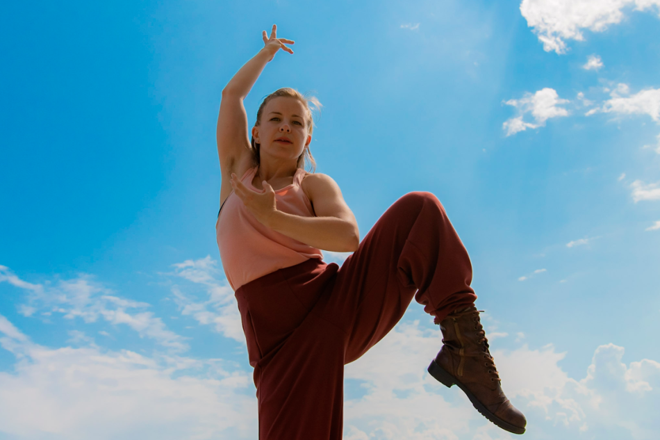 One person stands against a blue sky background with one hand and one leg up in the air