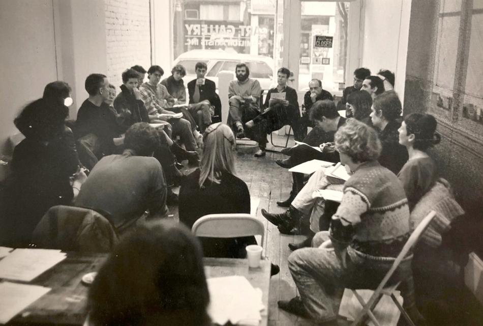 The image is a photo of  Annual general meeting of the Independent Artists Union at Hamilton Artists Inc., Nov. 29, 1987 by Cees van Gemerden. It's a black and white photo which shows a group of artists sitting in a circle on folding chairs in a crowded gallery space.