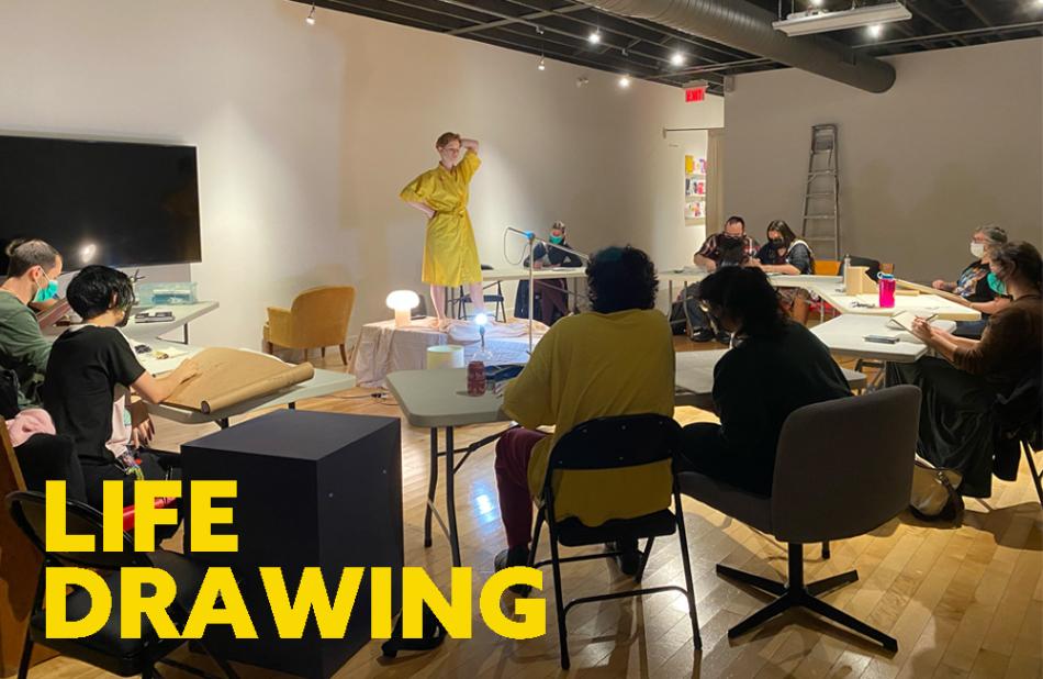 10 people are seated at tables in a circle drawing a model in a yellow robe standing in the center of the tables