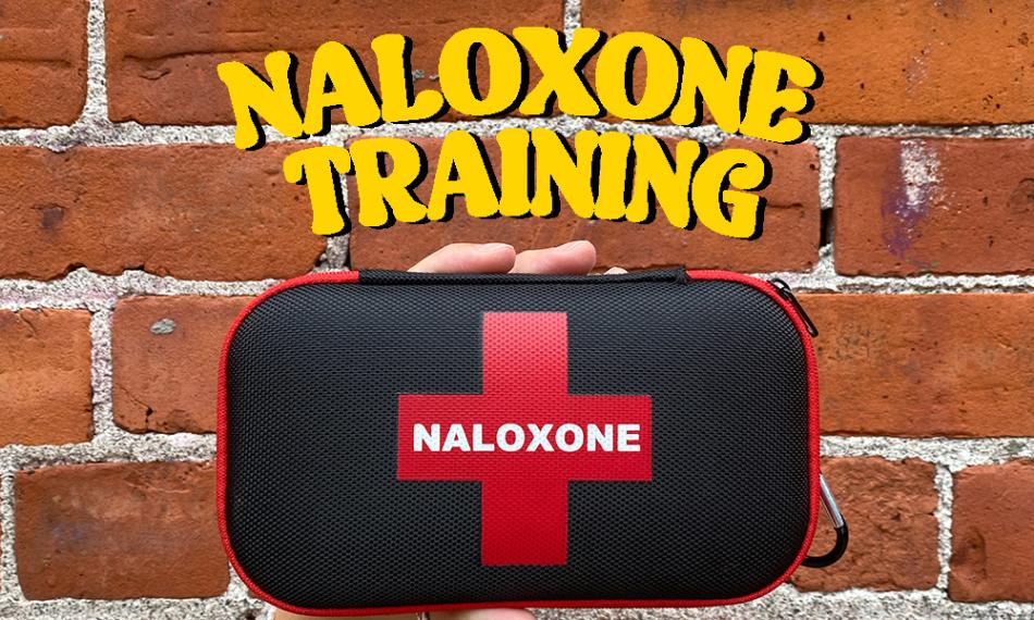 A photo of a red and black Naloxone kit in front of a red brick wall. It says "Naloxone Training" in bold yellow font at the top. 
