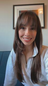 The photo is of Alexandria Holm, a woman with long brown hair, wearing a white shirt, and sitting on a blue couch.